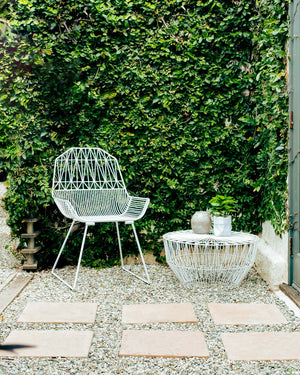 The Peacock lounge chair is a wire chair design made for both outdoor patio sets and indoor living room furniture. sisplayed here is the White lounge chair next to a fireplace in a modern home.